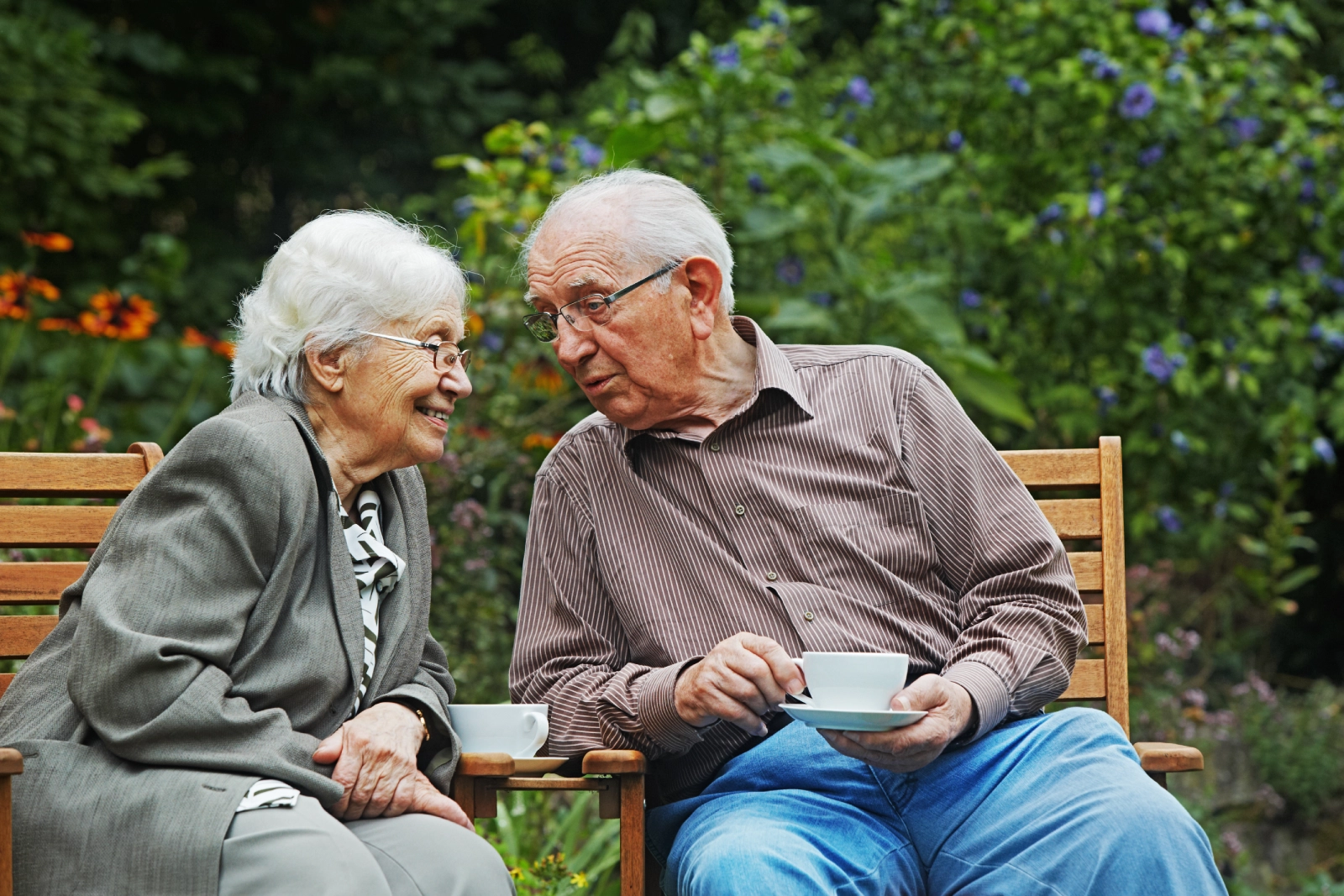 Senior couple sitting on a bench outdoors, talking and drinking tea.